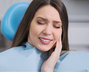 Young woman in dental chair holding cheek