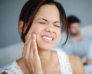 Woman grimacing in pain holds cheek