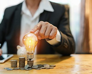 Person tapping a lightbulb that’s sitting on top of a stack of coins