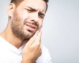 Bearded man in white shirt nursing a toothache