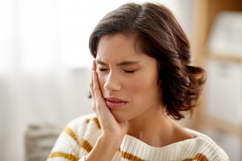 Brown-haired woman in sweater rubbing her jaw