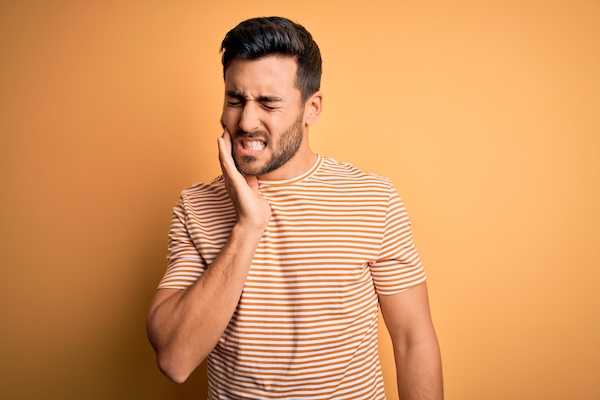 man grimacing with toothache against orange background