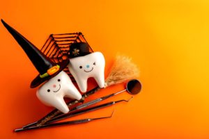 Two toy teeth with happy faces wearing Halloween costumes sitting on a fake broom with dental instruments